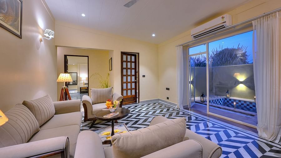 Cosy living room of Premium Suite Cottage with beige coloured sofas, a round coffee table, and patterned flooring, featuring large windows and serene evening lighting - Singhvilas, Ranthambore