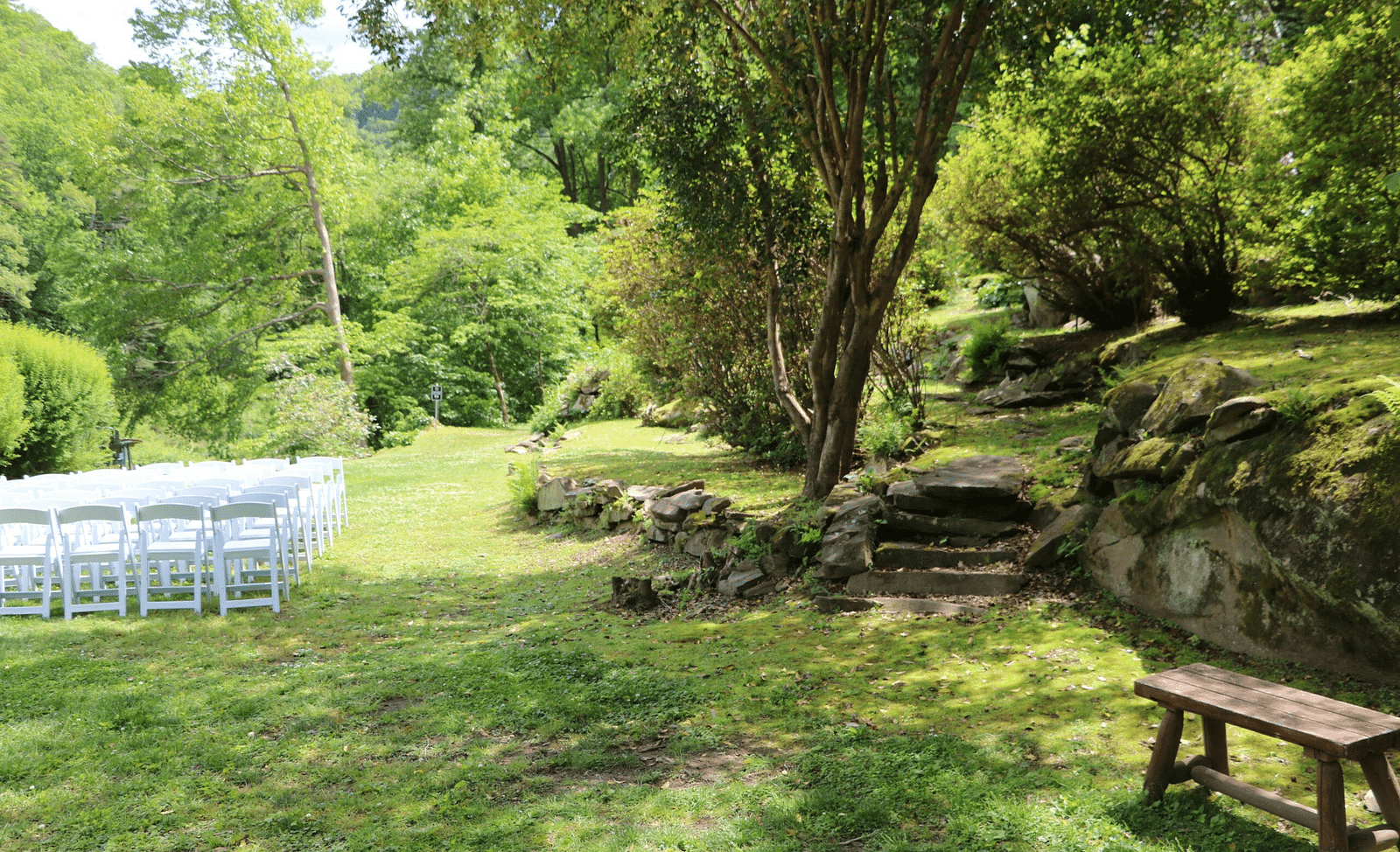a lush green lawn with white folding chairs arranged in a corner besides the tall green trees at the Riverside Lawn - Historic Tapoco Lodge