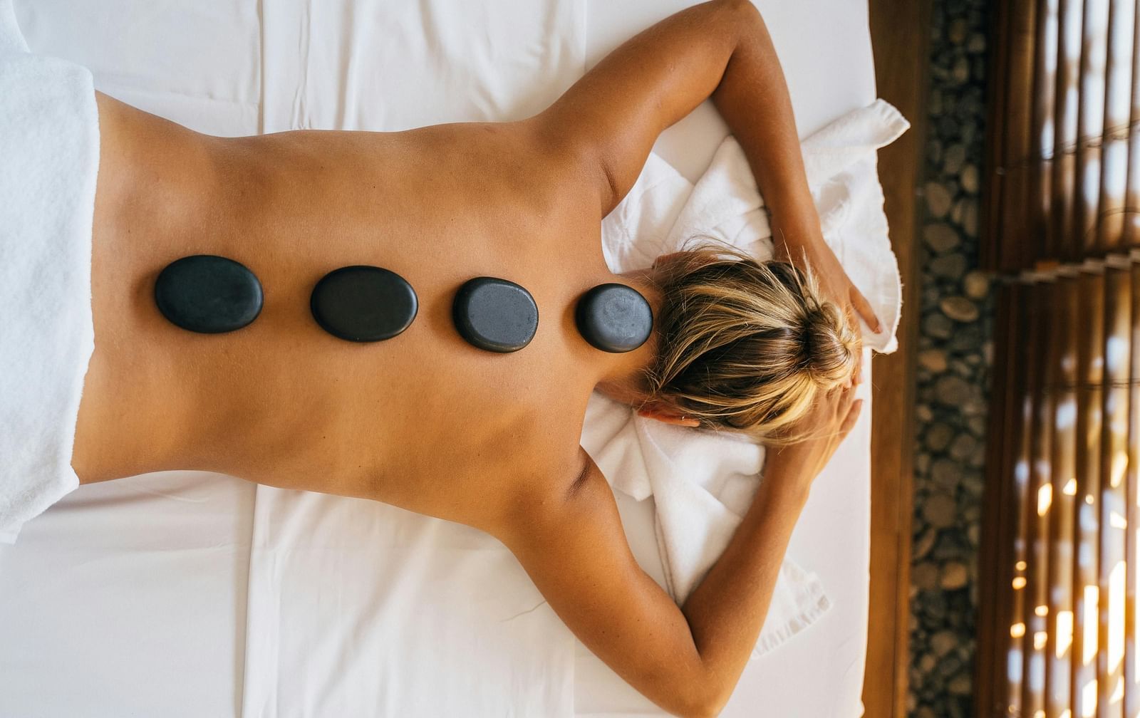 A woman lying down with back with black stones kept over her spine.