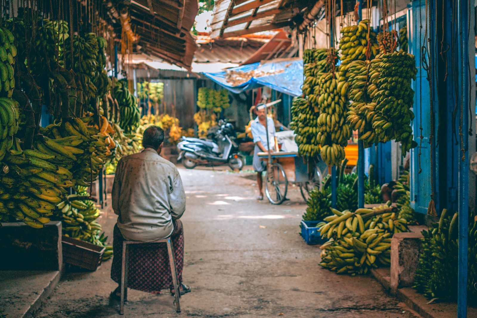 A person sitting outside a shop selling bananas
