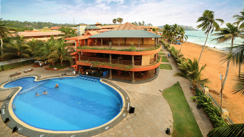 Uday Samudra Leisure Beach Hotel offers a swimming pool, tall buildings, swaying palm trees, and a sandy beach set against a clear blue sky