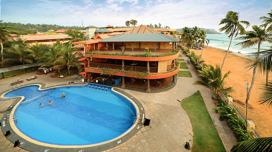 Uday Samudra Leisure Beach Hotel offers a swimming pool, tall buildings, swaying palm trees, and a sandy beach set against a clear blue sky