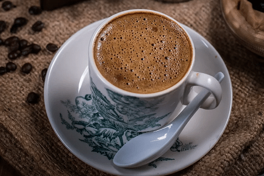 A cup of a drink on a saucer with a spoon.