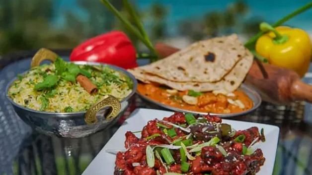 Variety of Indian dishes with vegetables, bread, and chutney, placed outdoors with a sea view | A Stone's Throw Away