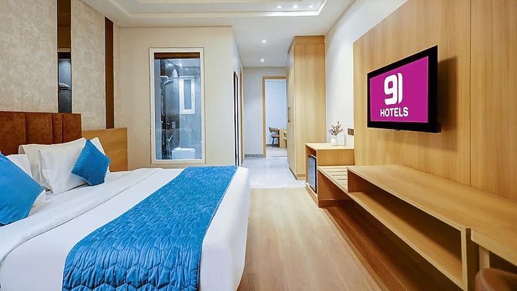 A bedroom at Hotel 91 HUDA Premier, Gurugram with a king size bed, pillows, wall-mounted TV, desk, and door.