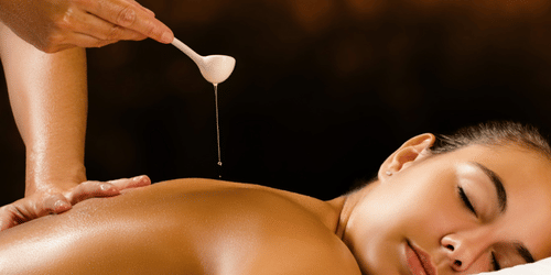 A spoon of liquid poured onto the upper back of a person lying with their eyes closed