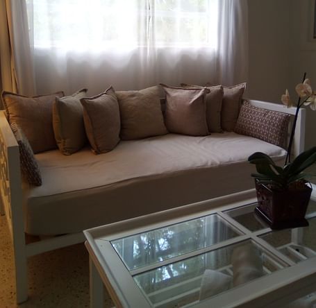 Lounge area at Casa Morada with a beige sectional sofa and a glass coffee table under a sheer curtained window.