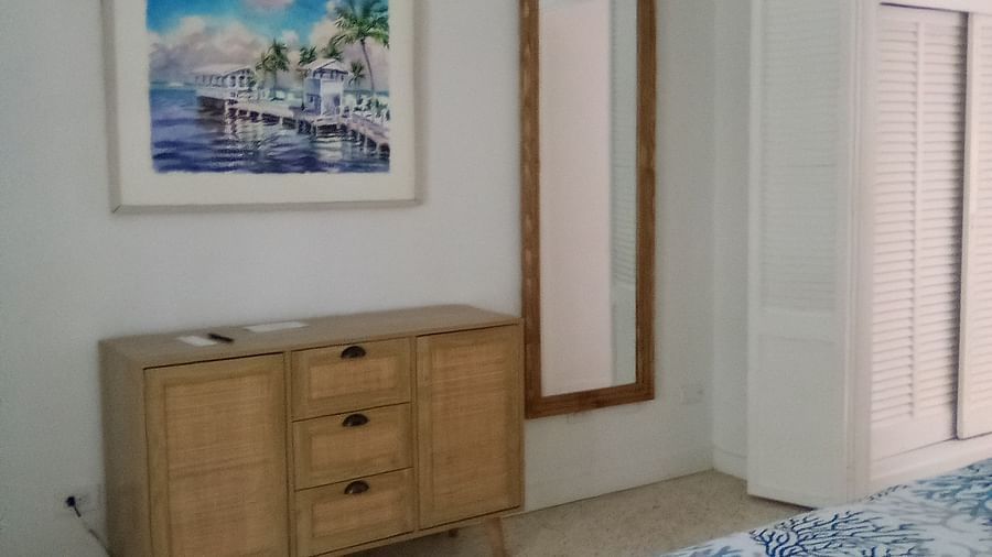 Bedroom at Casa Morada with a wooden dresser, framed wall art, and part of a bed with a patterned blue cover.