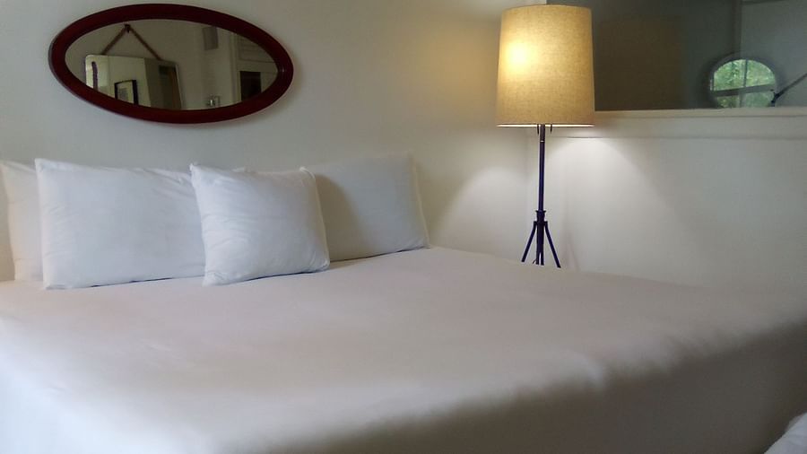 A single bed at Casa Morada with white bedding, a floor lamp, and an oval mirror mounted on the wall above the headboard.