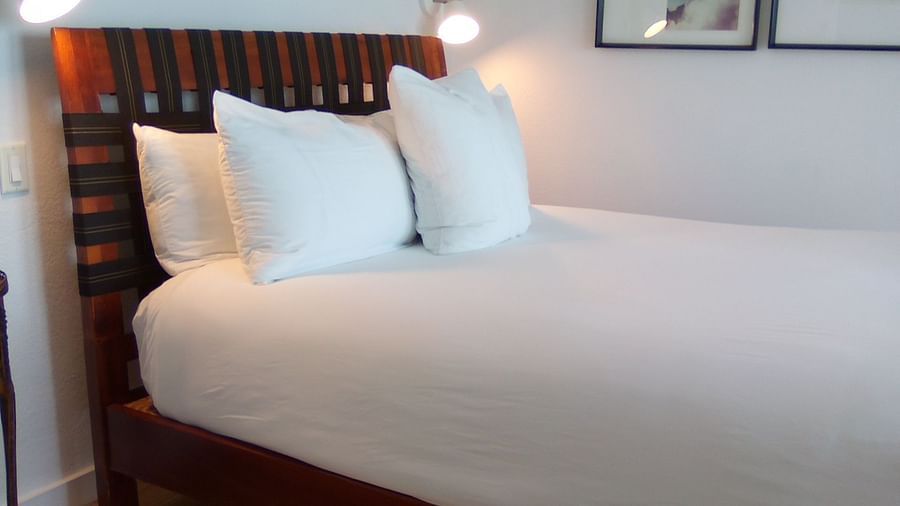 Bed with white linens and wooden headboard at Casa Morada, shown from a side angle.