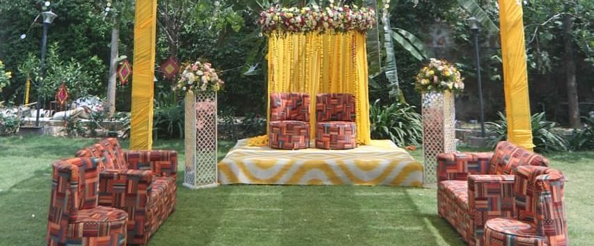 A decorated outdoor wedding setup at Tisya Farms, Gurgaon with yellow drapes, flags, and a ceremonial stage on a green carpet.