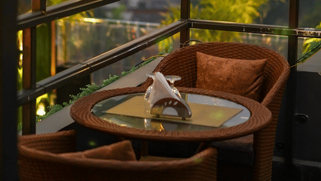 Two chairs facing each other on a terrace with warm lights besides it on a late evening.