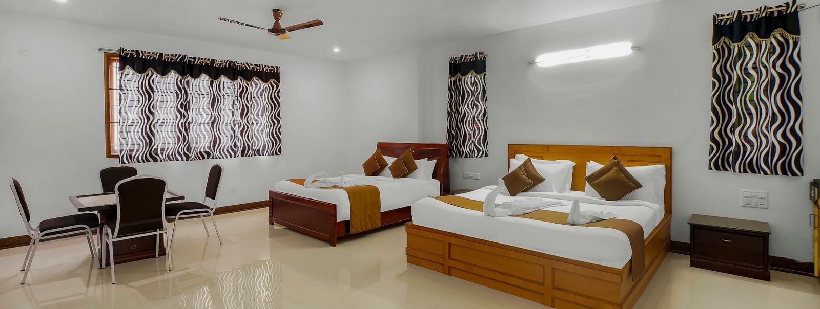 Spacious bedroom with two beds, a table with chairs placed around it and windows with a curtain at WOW Bungalow, Yercaud.
