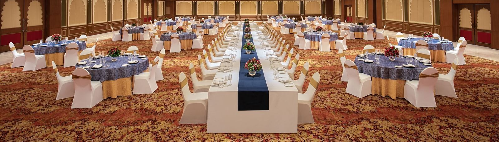 An image of a cosy event hall in Mahabalipuram with long and round tables, chandeliers, and carpeted floors – Kaldan Samudra Palace, a Luxury Wedding Hall in ECR