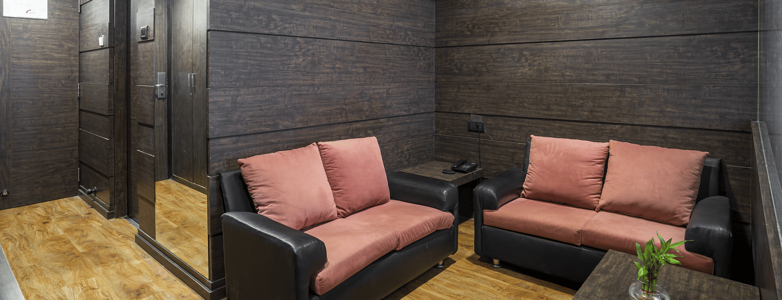 Room with two sofas, a table and dark wall panels at Infiniti Hotel, Indore.