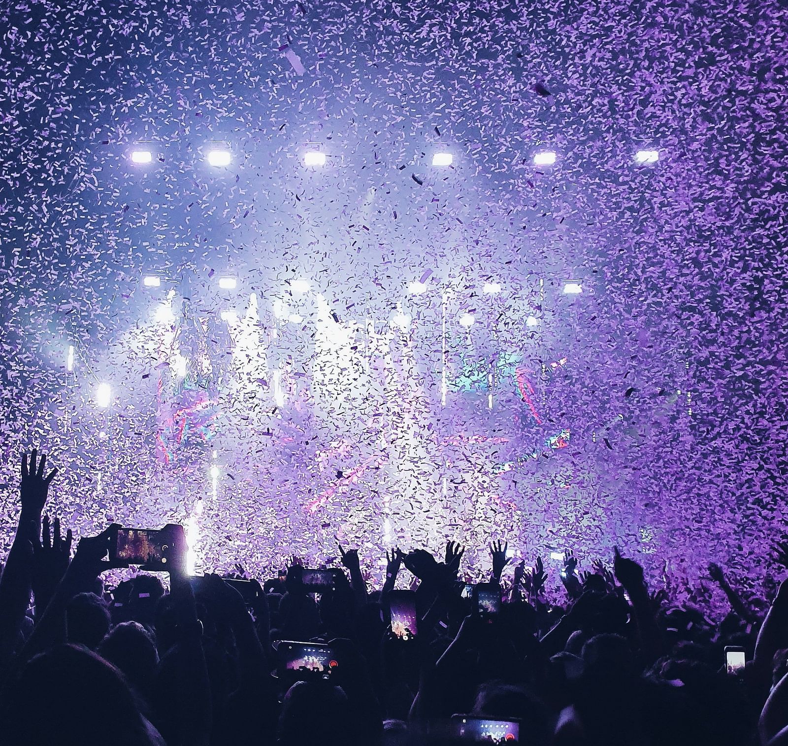 Concert lights illuminate the stage, with the crowd's silhouettes framed around it