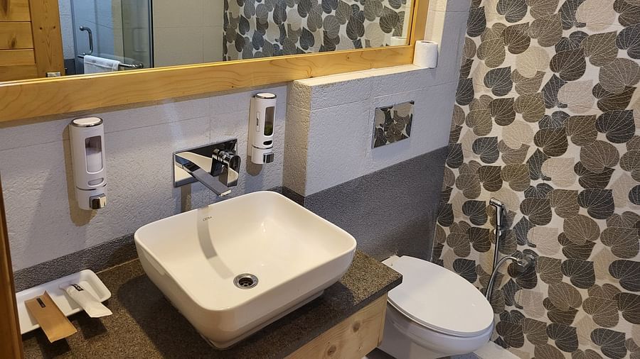 A stylish bathroom with a white vessel sink, patterned wallpaper, and a large mirror at Dagshai Manor Kasauli - Inde Hotels.