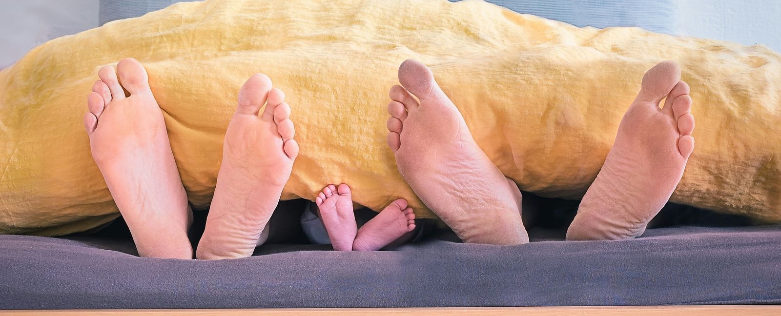 A picture showing the feet of parents and a child under the covers sleeping on a bed