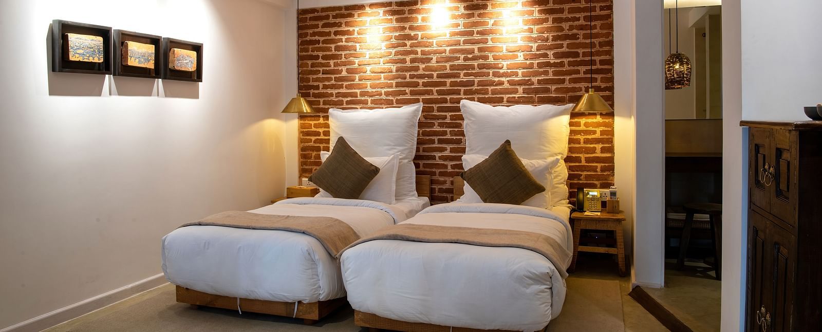 The room at The Nanee includes twin beds, bedside tables with lamps, and three pieces of artwork displayed on the wall.