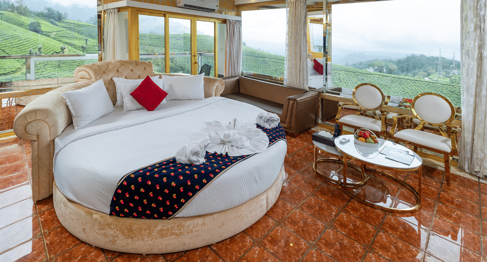 An interior view of the Jacuzzi 180-degree Suite at Parakkat Nature Hotel and Resorts, Munnar, featuring a large round bed, plush decorative pillows, and elaborate gold-toned ceiling accents.
