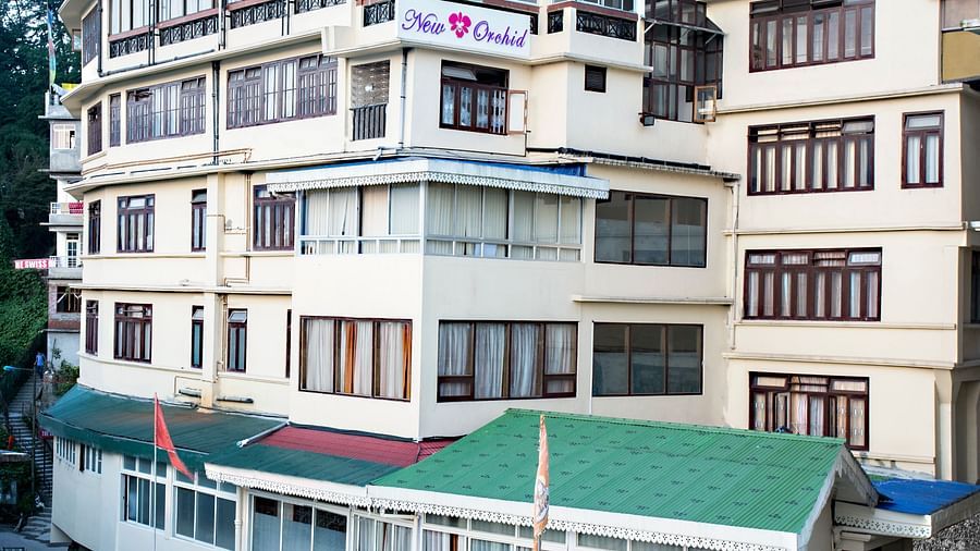 The exterior of New Orchid Lords Inn Gangtok  is shown during the daytime, nestled on a hillside with multiple stories and windows.
