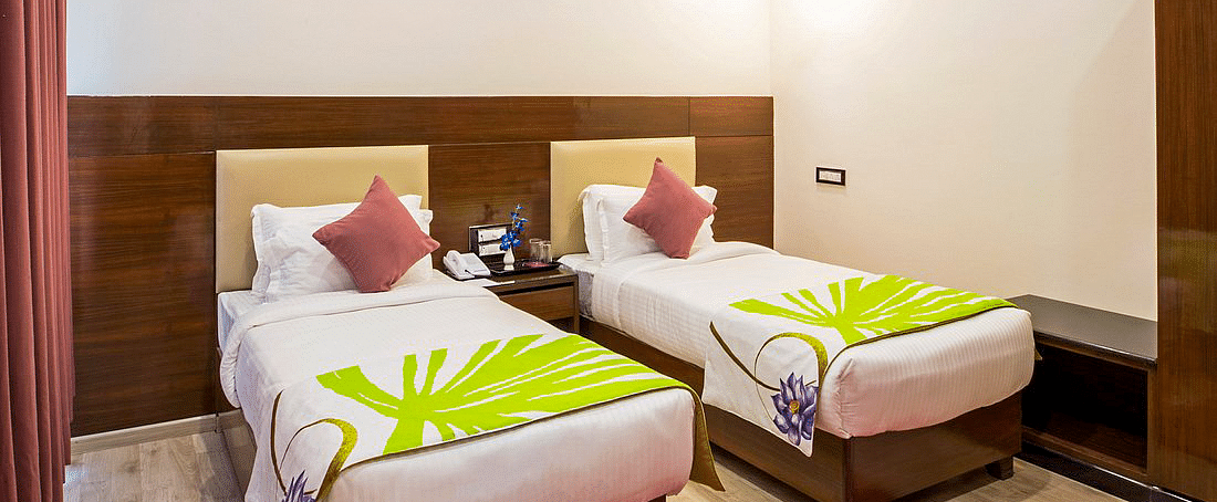 Corner view shot of the Deluxe Twin Room at Regenta Inn DLS featuring two single beds along with a bright red carpet on the floor.