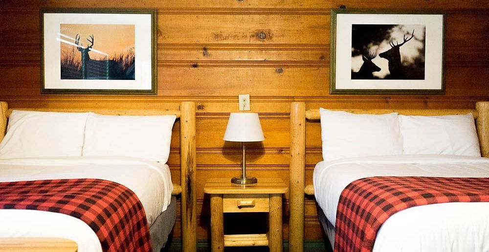 A wooden cabin with twin beds and a side table with a night lamp placed between them at Shaver Lake Village Hotel.