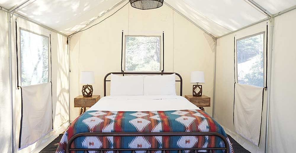 A tent with zip-down windows and a double bed placed in the middle at Shaver Lake Village Hotel.