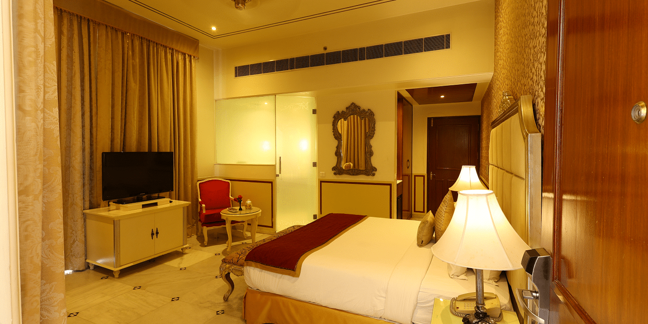 Image of a room with a bed, a television in front and lamps on the side of the bed at Rajasthali Resort & Spa Jaipur.
