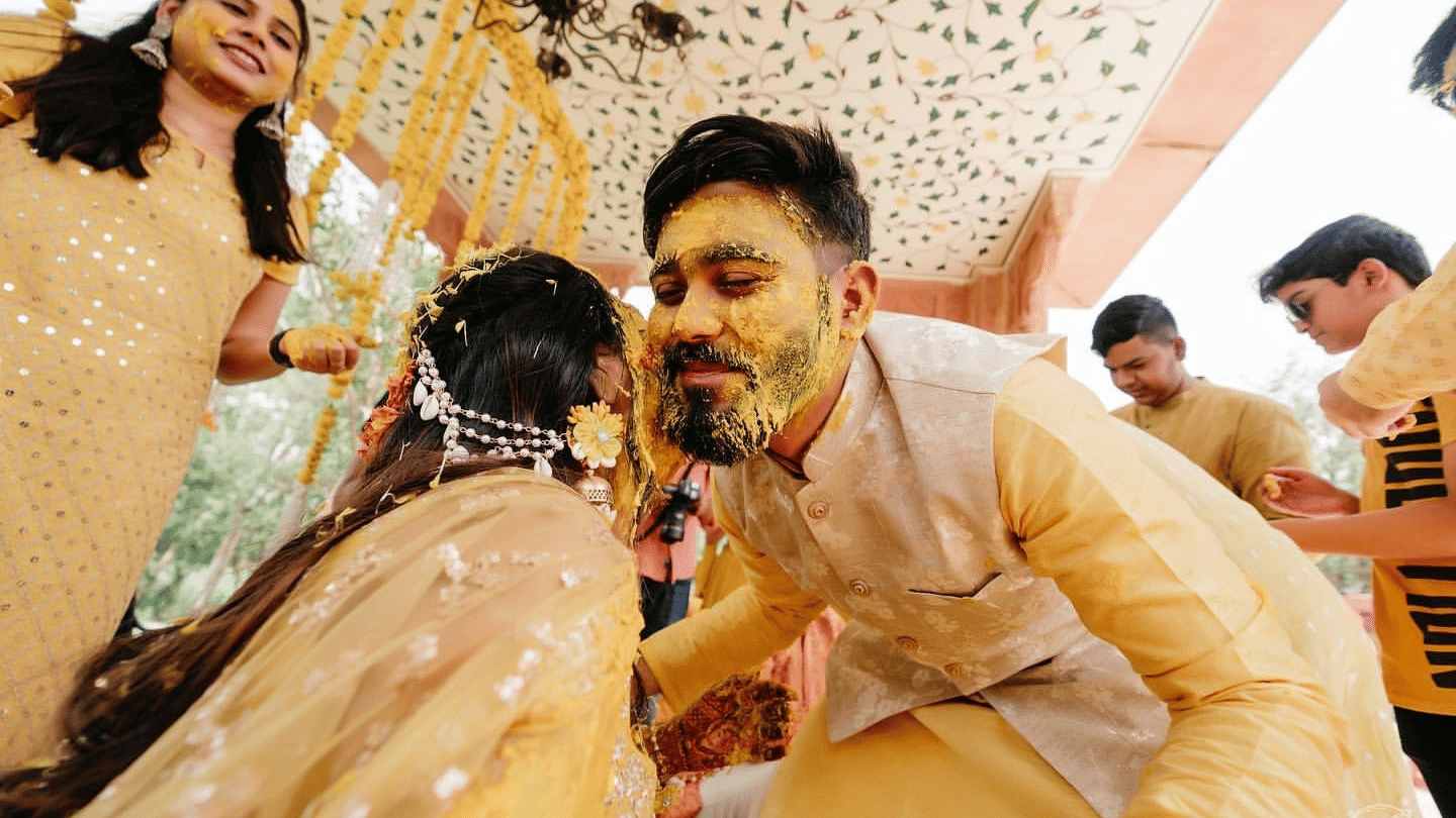 A groom with turmeric-covered face leans in playfully towards his bride during a joyful haldi ceremony, surrounded by loved ones at Umaid Palace, one of the royal wedding venues in Jaipur.