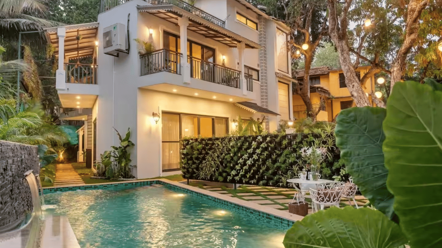 Villa exterior of Lime Tree Hotels & Service Apartment Private Limited featuring a swimming pool, lush greenery, and evening lighting along the pathway.