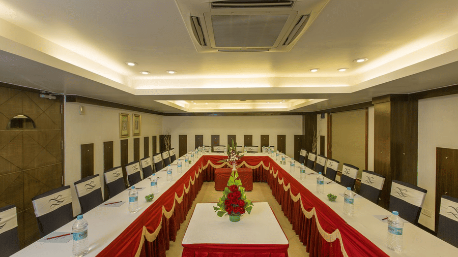 Banquet hall at The Citrine, Bangalore set in U-shape with red and gold table skirting, floral centrepieces and ceiling-mounted AC unit.