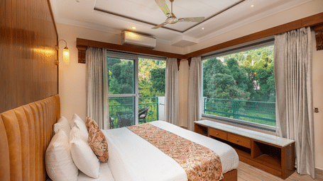 A bedroom with a bed and large wall to wall windows overlooking trees, and a balcony at Quality Inn.
