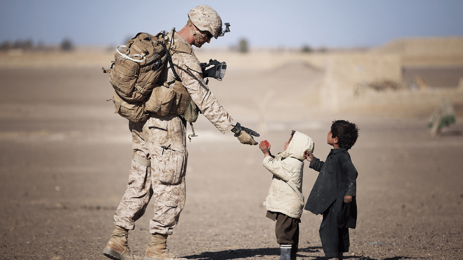 A soldier in an arid region handing over relief supplies to a small toddler