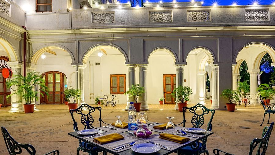 4 metal chairs with a set table and the palace in the background - The Baradari Palace