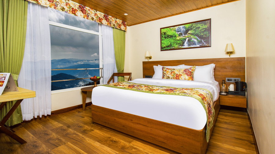 Deluxe Room featuring wooden interiors, king size bed, large window with views of hills, and cosy seating making it one of the best places to stay in Darjeeling | Mount Lungta Boutique Hotel & Spa