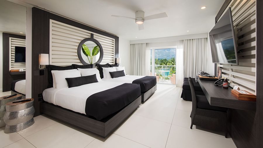 A image of a hotel room with twin beds, a balcony offering sea views, and a wall-mounted television - S Hotel Montego Bay, Jamaica