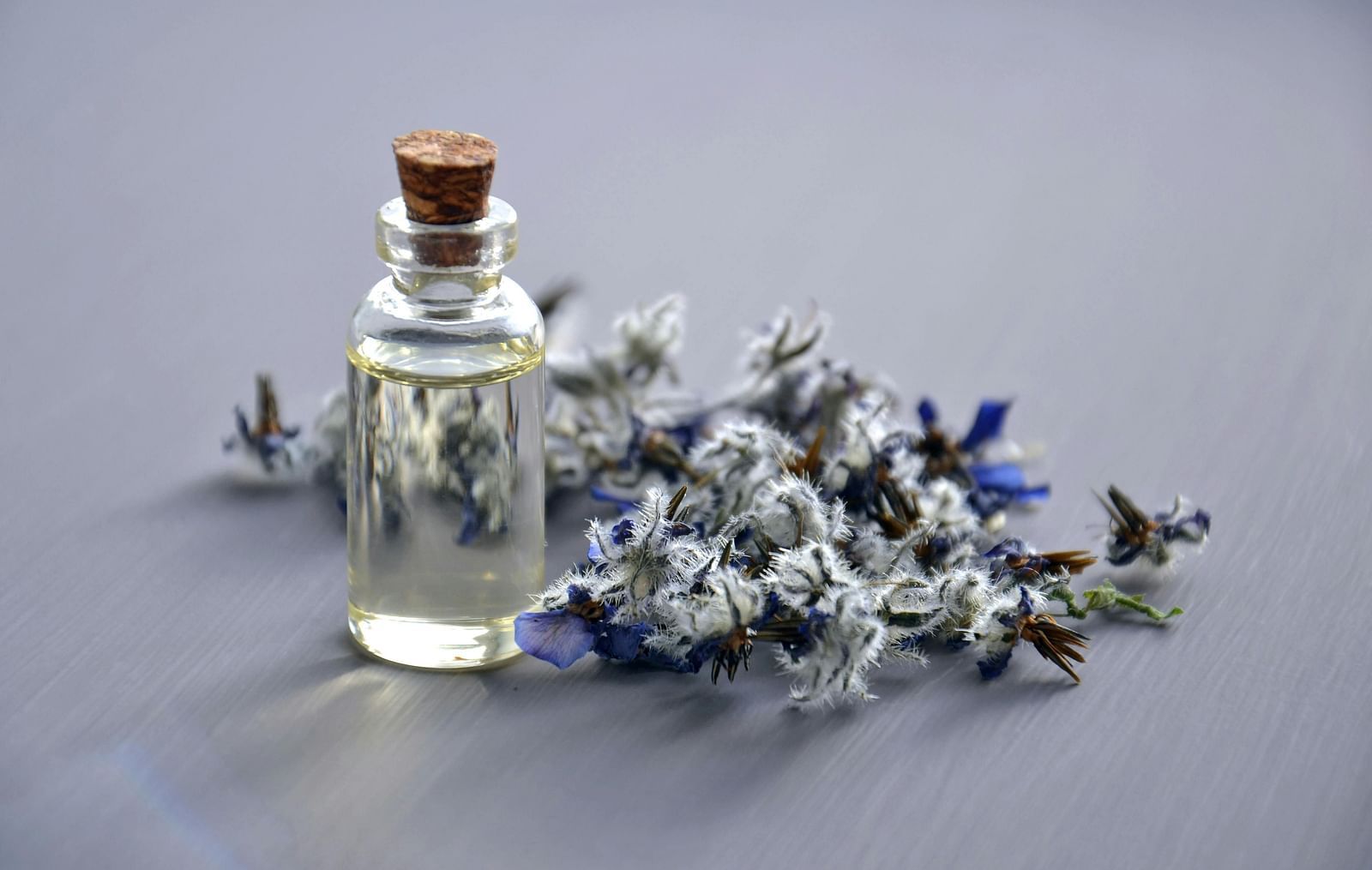 A close-up displays homeopathic remedies, including a bottle of pills, white globules, and a sprig of lavender, alongside a smooth stone on a reflective black surface.