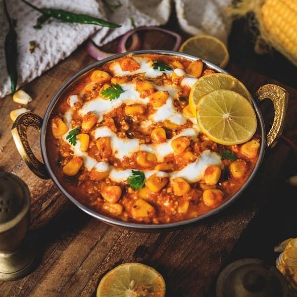 A round metal dish filled with a creamy curry, topped with white swirls and cilantro, and garnished with lemon slices, sits on a rustic wooden surface.