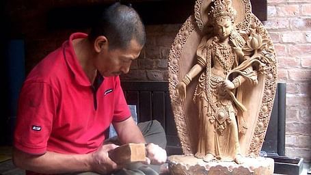 An overview of a man sculpting an idol from wood with accurate hits of the hammer.