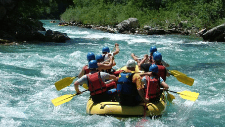A group of people wearing life jackets and helmets paddling a yellow raft through whitewater rapids on a river.