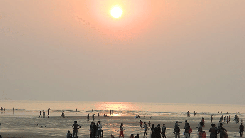 An image of the sun setting over the sea with people walking along the shore.