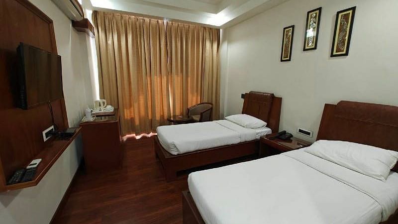 A spacious Luxury Room with two single beds along with beige coloured curtains covering the windows - Hotel Gold, Panipat