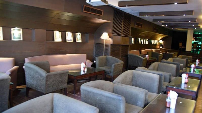 Several grey coloured cushioned arm chairs placed in front of individual tables with a projector hanging from the ceiling at 24 Karats Bar - Hotel Gold, Panipat
