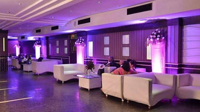 Corner view shot of the 24 Karats bar with people sitting on the sofas and violet halogen lights lit in the corner - Hotel Gold, Panipat