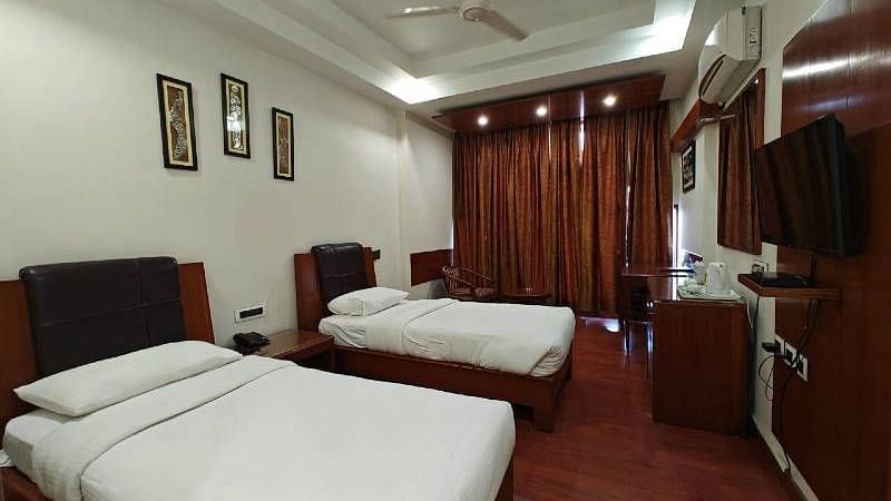 A bedroom with two single beds and dark wooden flooring along with a wall mounted television - Hotel Gold, Panipat