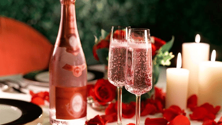 A bottle of pink champagne with two glasses surrounded by rose petals.