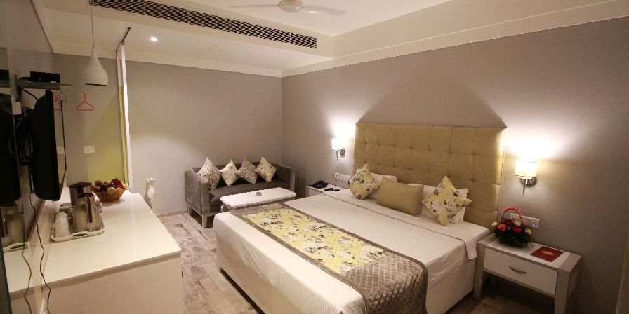 Elegant room with a large bed, bed side table, sofa, and TV unit at Hotel Emerald, Chandigarh