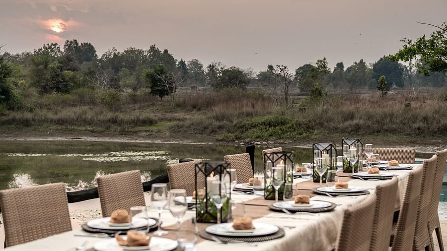 A dining table and multiple chairs arranged neatly near pool at Saccharum Safari Lodge, Balaghat