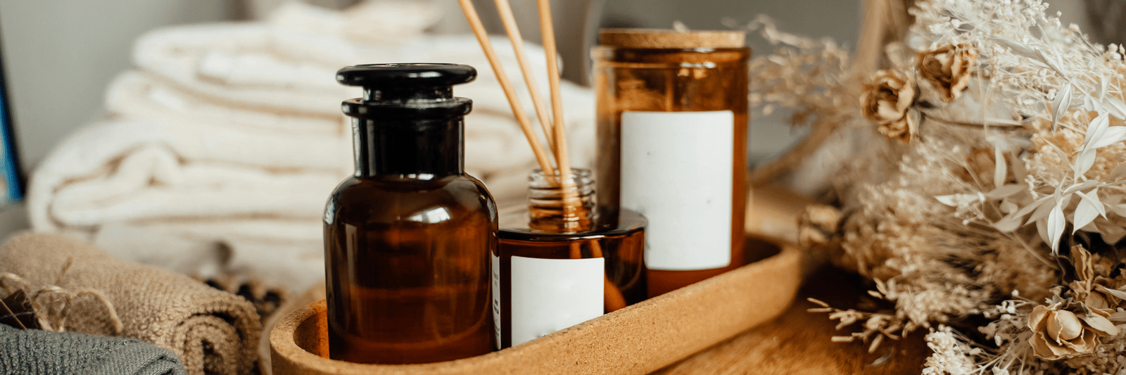 A tranquil arrangement of folded towels, amber glass bottles, and wooden diffuser sticks on a tray.